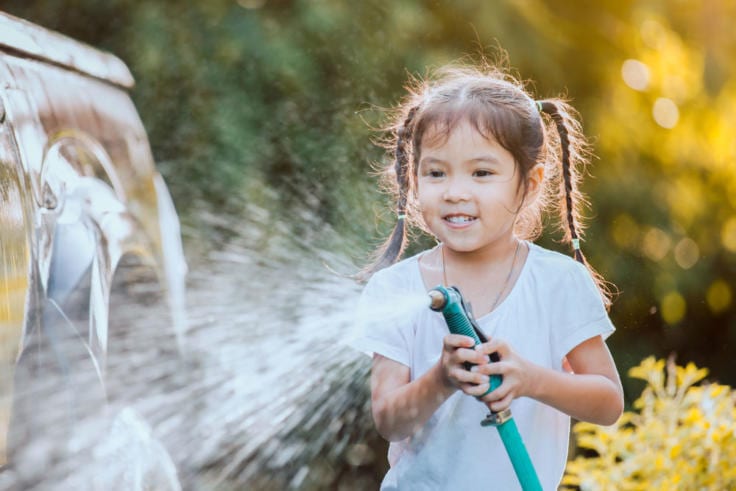 Child washing car using lawn hose